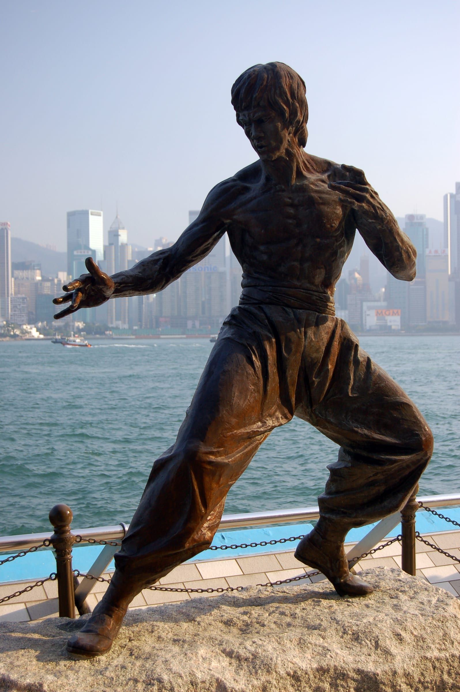 Bronzestatue von Bruce Lee in Kampfhaltung an der Avenue of Stars in Hongkong, im Hintergrund der Victoria Harbour